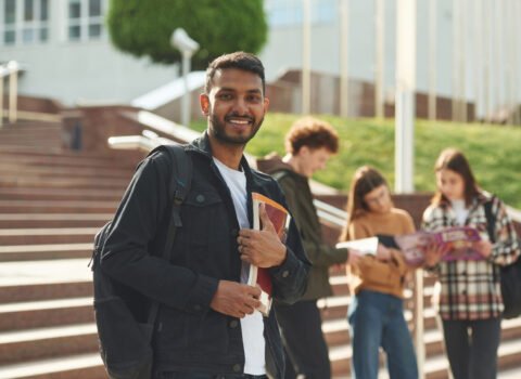 Indian man is standing in front of his friends. Four young students in casual clothes are together outdoors