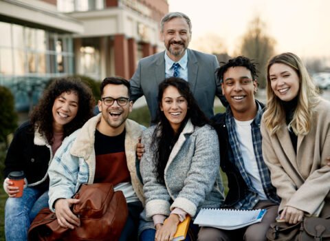 Portrait of happy mature professor with group of his students at campus.