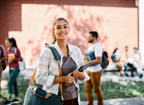 Young happy student standing at campus and looking at camera.